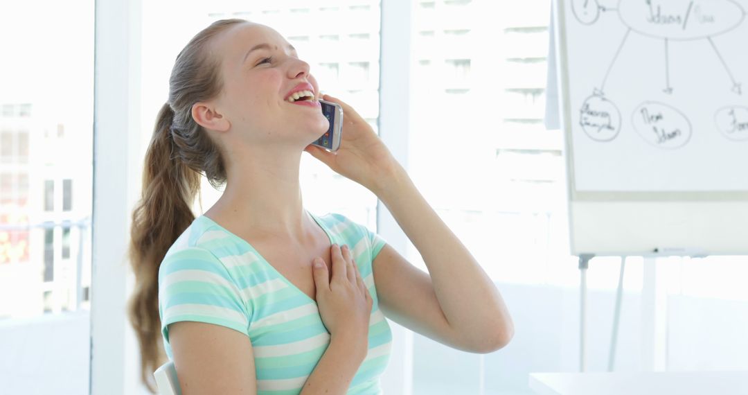 Young Woman Laughing While Talking on Phone in Bright Office - Free Images, Stock Photos and Pictures on Pikwizard.com