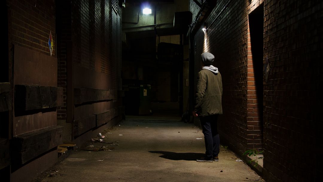 Person Standing in Dark Alley at Night Near Dim Light - Free Images, Stock Photos and Pictures on Pikwizard.com