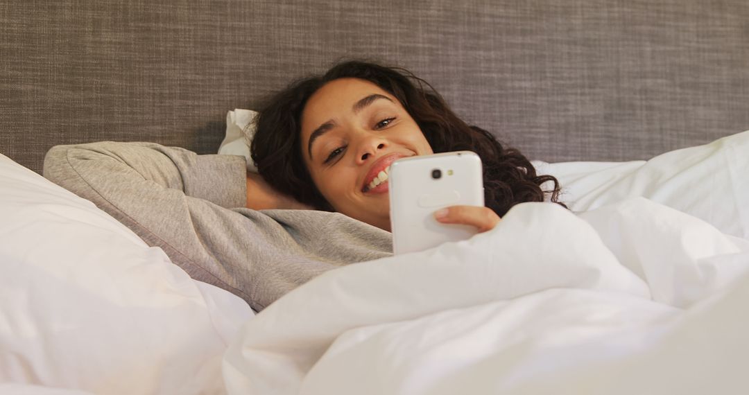 Smiling Woman Relaxing in Bed While Browsing Smartphone - Free Images, Stock Photos and Pictures on Pikwizard.com