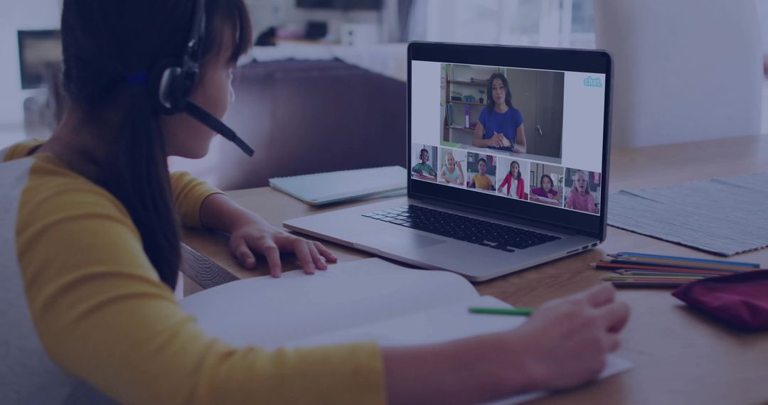 Young girl studying online with headset and laptop at home desk taking notes in virtual classroom