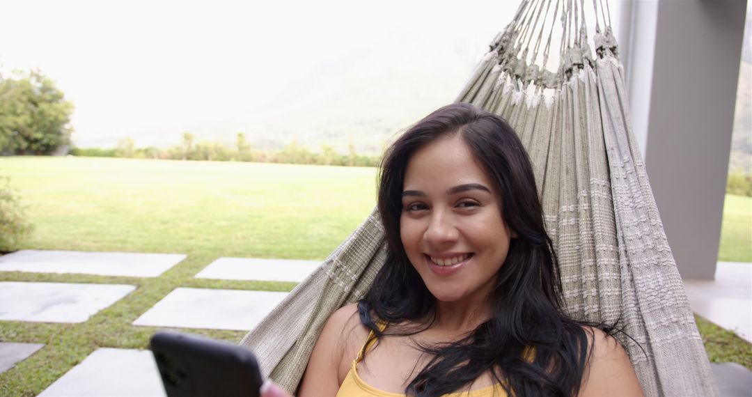 Young Woman Relaxing in Hammock with Smartphone in Backyard