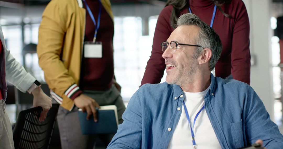 Mature man in wheelchair smiling as diverse coworkers guide and collaborate in open office