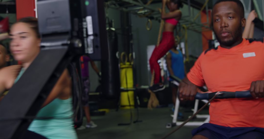 Focused Man Exercising on Rowing Machine in Busy Gym