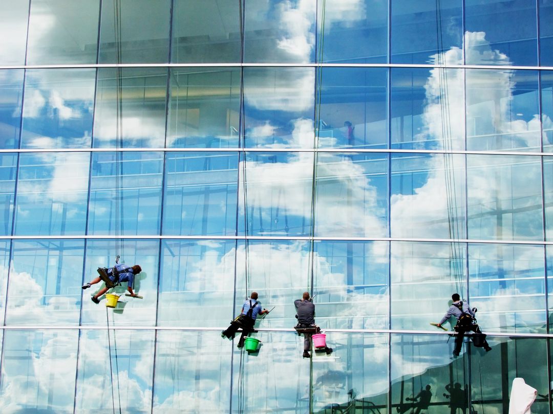 Workers Cleaning Glass Facade of Modern Building Reflecting Blue Sky and Clouds - Free Images, Stock Photos and Pictures on Pikwizard.com