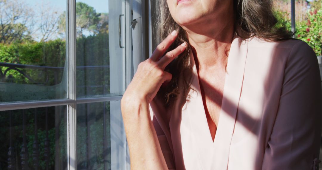 Pensive Mature Woman Gazing Out of Window in Sunlight - Free Images, Stock Photos and Pictures on Pikwizard.com