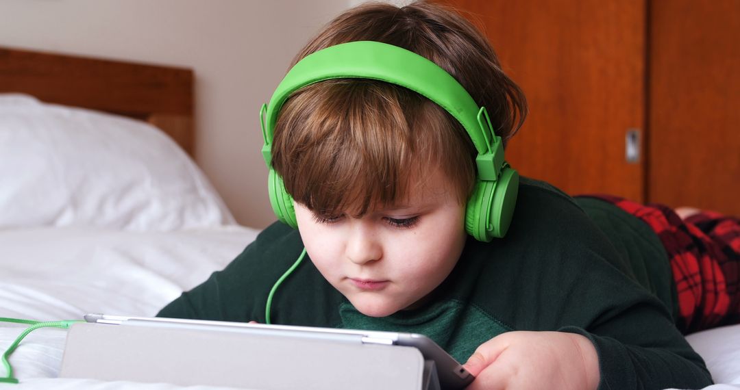 Young Boy Wearing Green Headphones Browsing Tablet on Bed - Free Images, Stock Photos and Pictures on Pikwizard.com