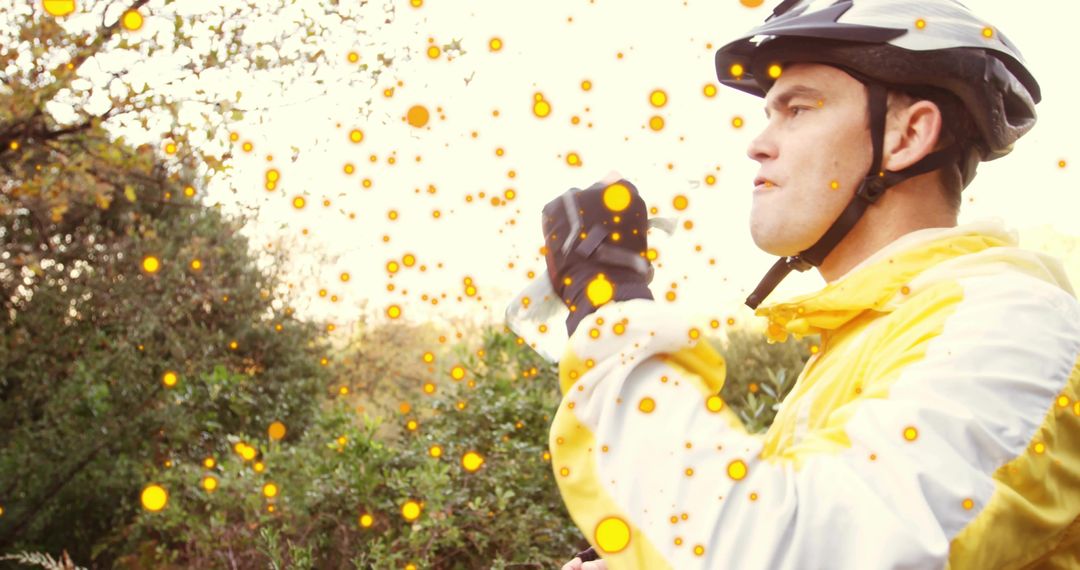 Cyclist drinking water on wooded trail wearing yellow jacket and helmet, taking hydration break
