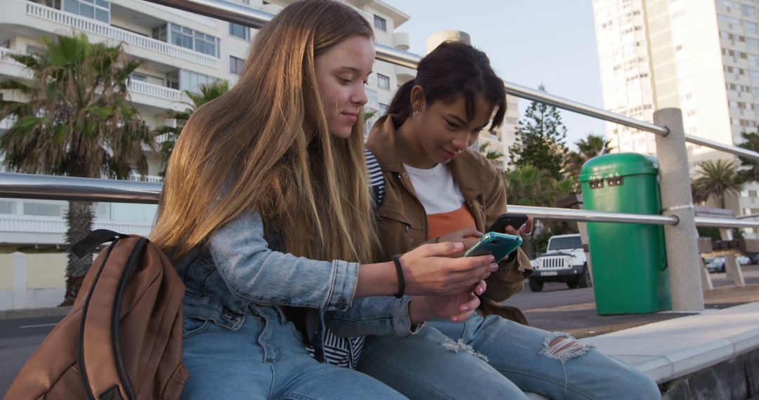 Two Young Women Looking at Smartphone While Sitting Outdoors - Free Images, Stock Photos and Pictures on Pikwizard.com