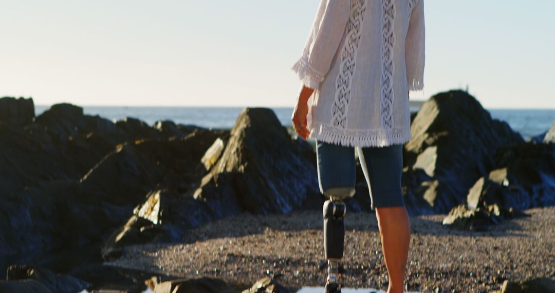 Woman with Prosthetic Leg Walking on Rocky Beach at Sunset - Free Images, Stock Photos and Pictures on Pikwizard.com