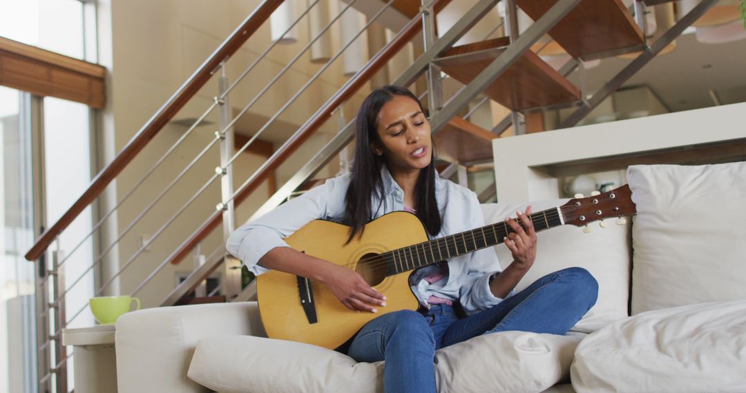 Young woman playing guitar on a cozy couch in a modern living room - Free Images, Stock Photos and Pictures on Pikwizard.com