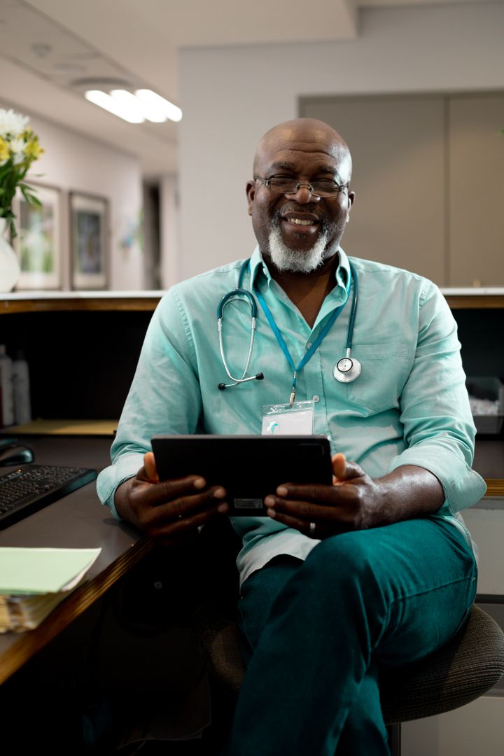 Smiling Senior African American Doctor Holding Tablet in Hospital Reception - Free Images, Stock Photos and Pictures on Pikwizard.com