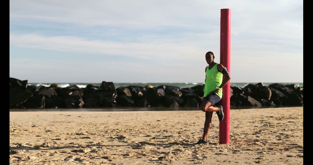 Jogger Adjusting Arm Band on Beach Near Rocky Shoreline
