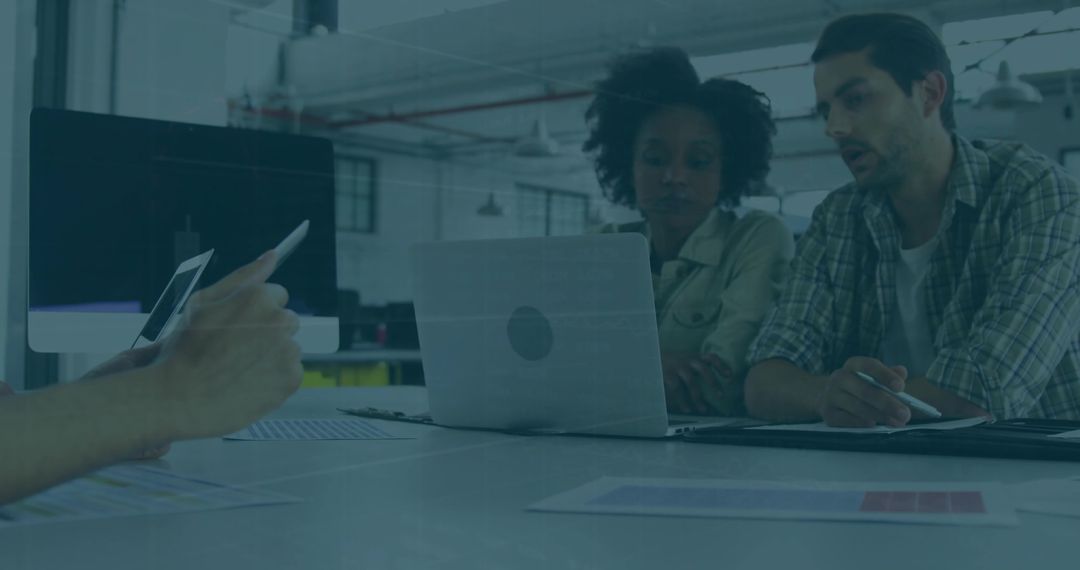 Collaborating team reviewing charts on laptop in open-plan coworking industrial workspace