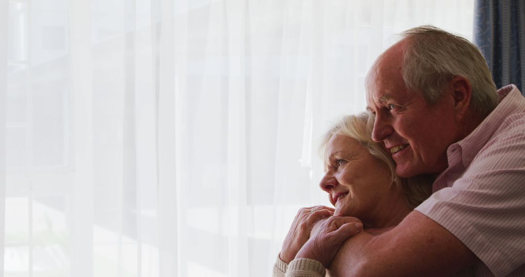 Senior Couple Embracing and Smiling by Window Light