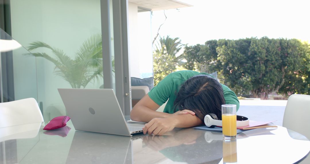 Exhausted Student Napping Near Laptop and Juice in Sunlit Room