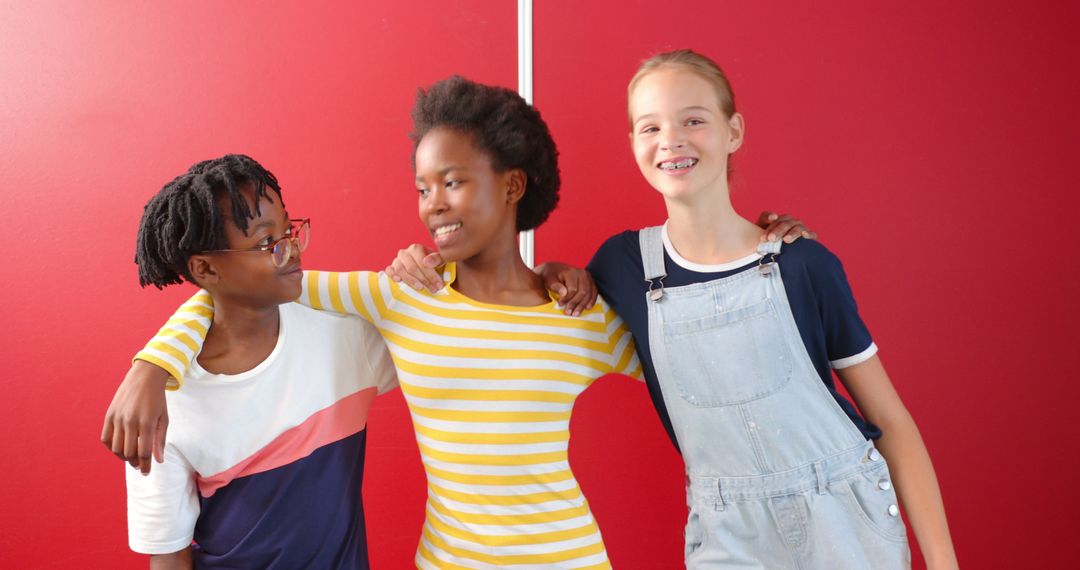 Three Diverse Girls Embracing in Front of Red Wall with Joyful Expressions