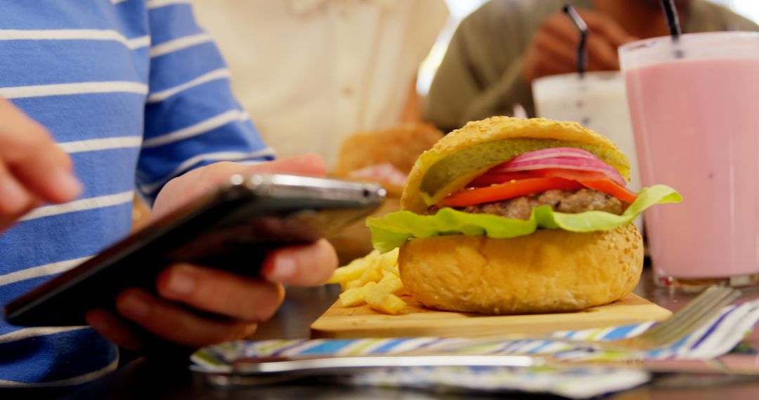 Teen Using Smartphone While Eating Burger at Diner - Free Images, Stock Photos and Pictures on Pikwizard.com