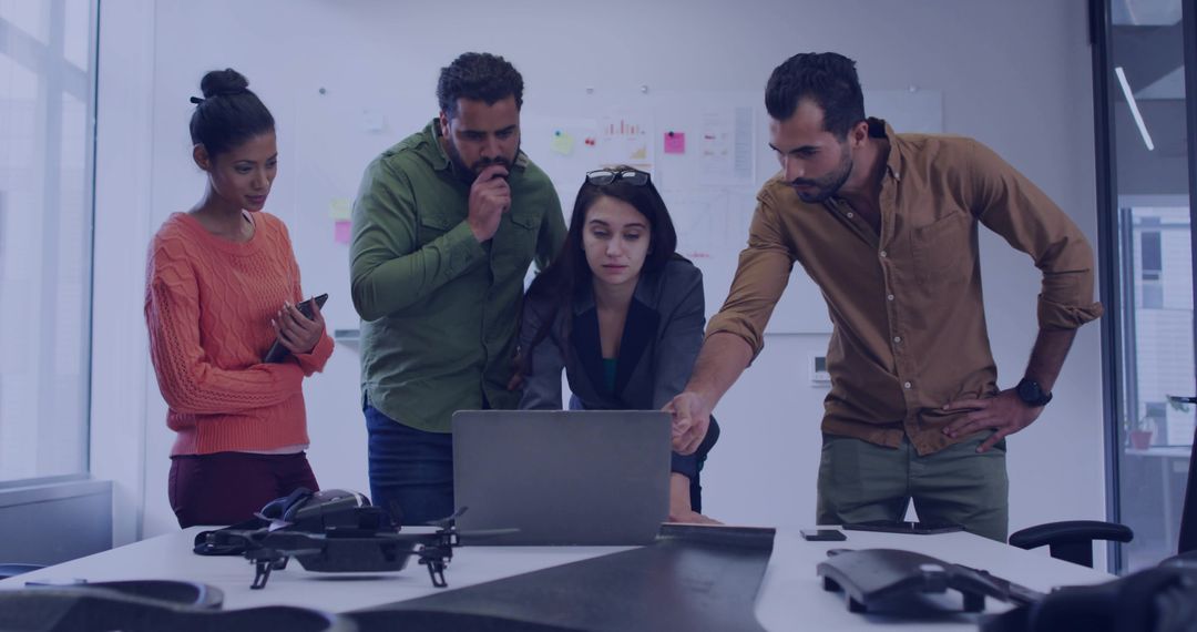 Multicultural Team Collaborating on Drone Prototype Around Laptop in Modern Startup Office