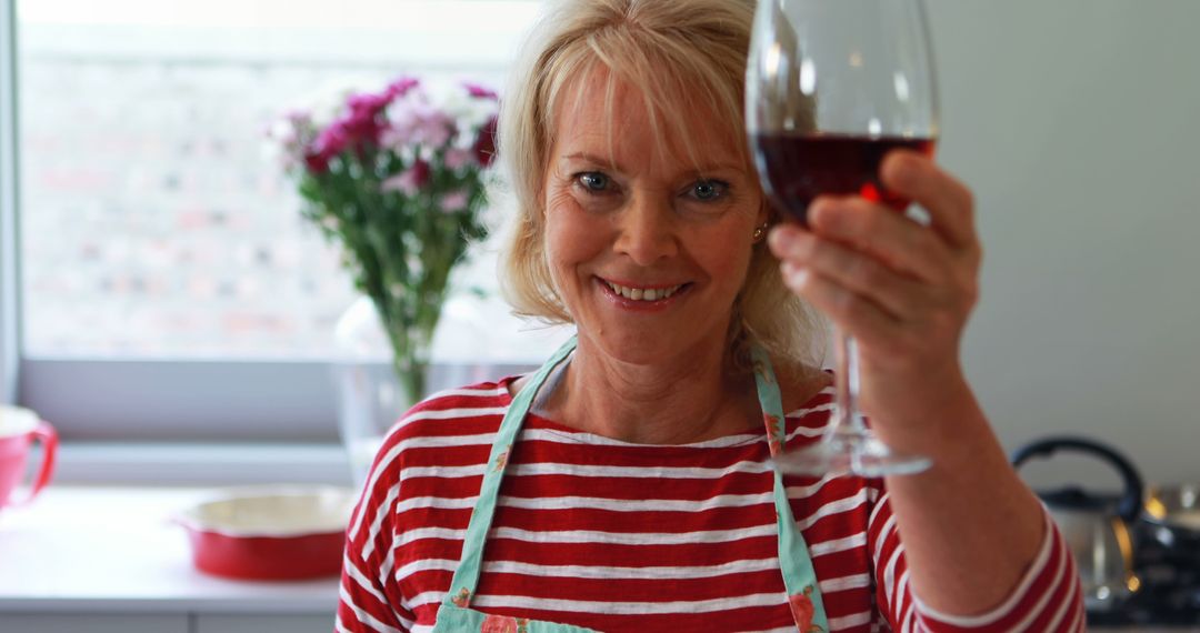 Smiling Senior Woman Raising Glass of Red Wine in Home Kitchen - Free Images, Stock Photos and Pictures on Pikwizard.com