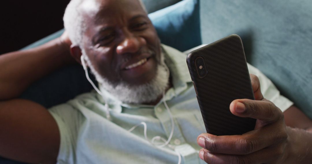 Elderly Man Relaxing on Couch Watching Smartphone with Earbuds - Free Images, Stock Photos and Pictures on Pikwizard.com