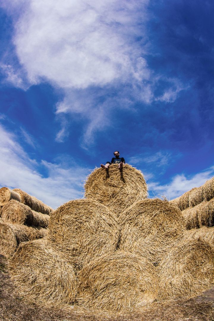 Person sitting on large pile of hay bales under blue sky - Free Images, Stock Photos and Pictures on Pikwizard.com