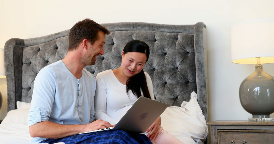 Interracial Couple Smiling and Using Laptop in Bedroom - Free Images, Stock Photos and Pictures on Pikwizard.com