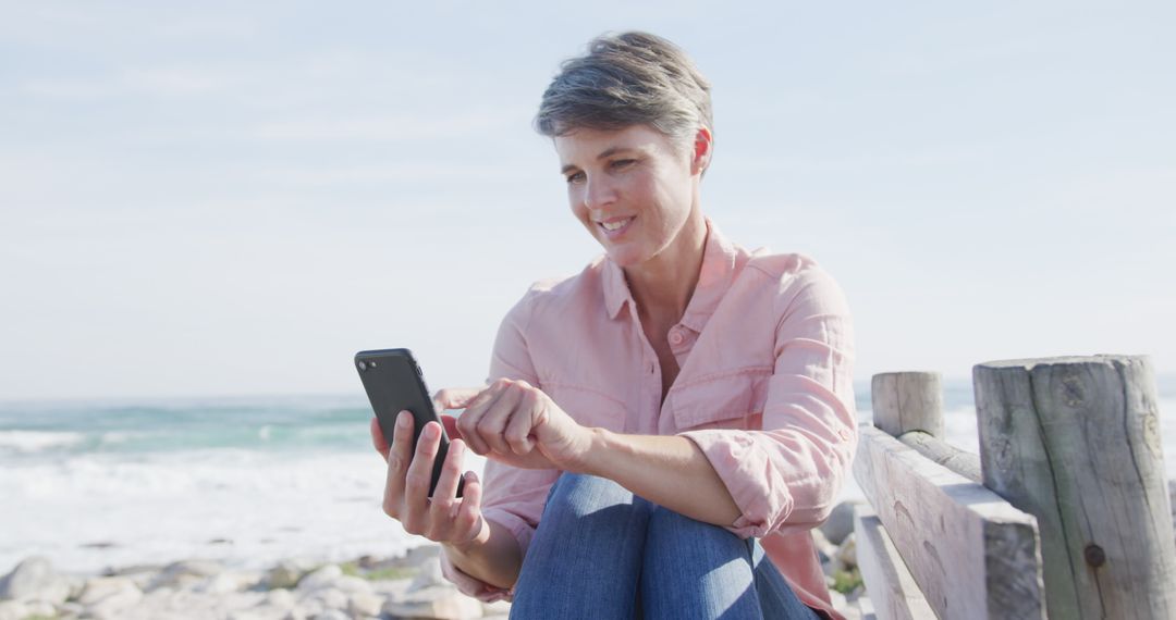 Smiling Woman Using Smartphone by Ocean - Free Images, Stock Photos and Pictures on Pikwizard.com