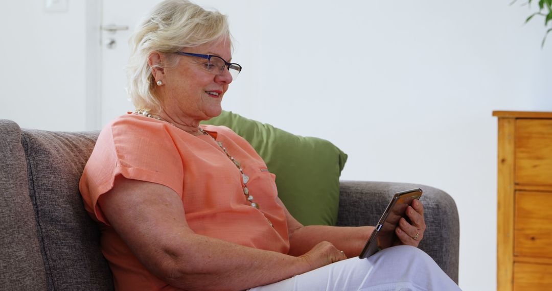 Senior Woman Sitting on Sofa Using Tablet, Smiling - Free Images, Stock Photos and Pictures on Pikwizard.com