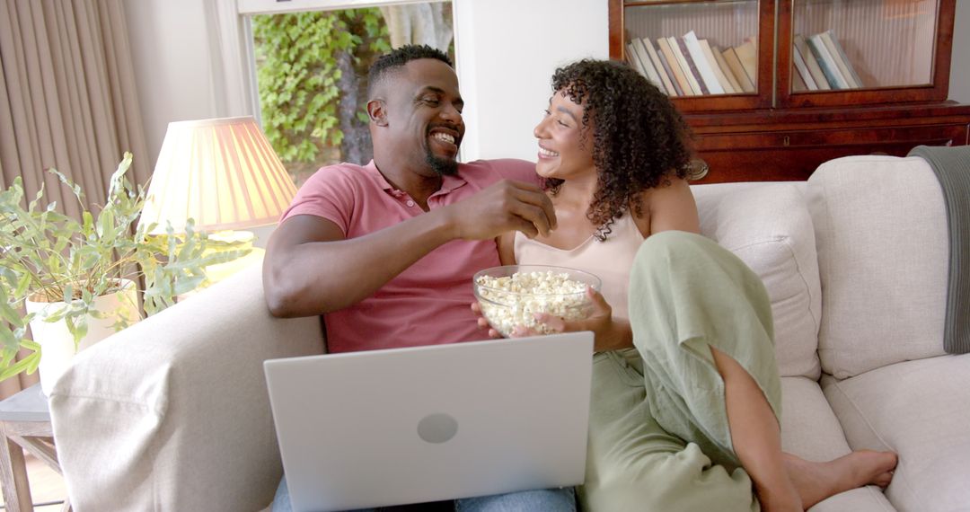 Happy Couple Relaxing on Couch Sharing Popcorn and Laptop