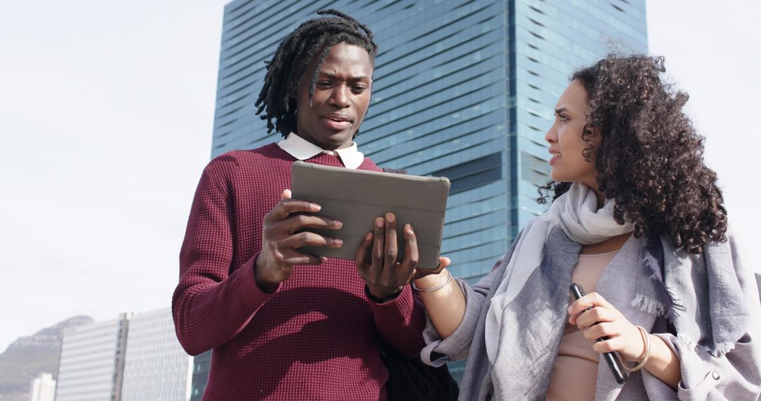 Diverse coworkers consulting tablet with stylus outside glass tower in downtown plaza
