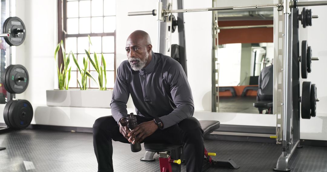 Senior Man Resting on Gym Bench with Shaker in Modern Fitness Center