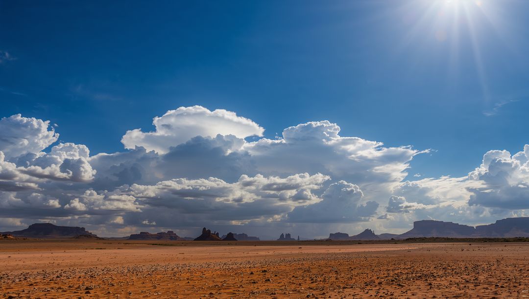 Sunburst over endless red desert with dramatic towering clouds and distant sandstone mesas
