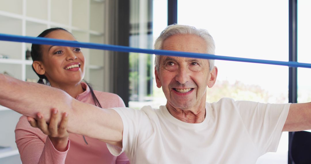 Smiling elderly man stretching with resistance band assisted by a caregiver - Free Images, Stock Photos and Pictures on Pikwizard.com