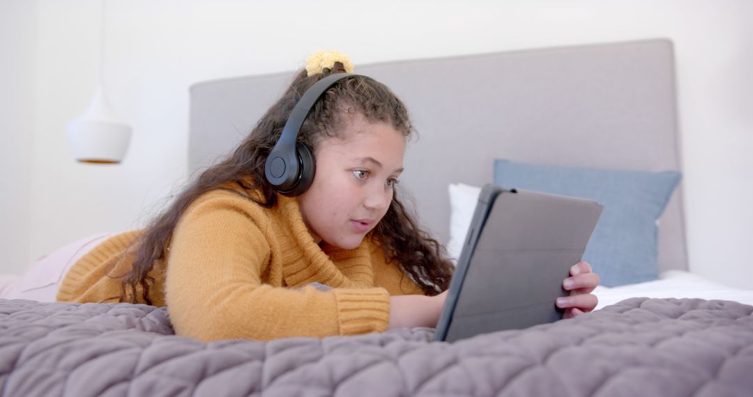 Biracial Girl Relaxing on Bed with Tablet and Headphones - Free Images, Stock Photos and Pictures on Pikwizard.com