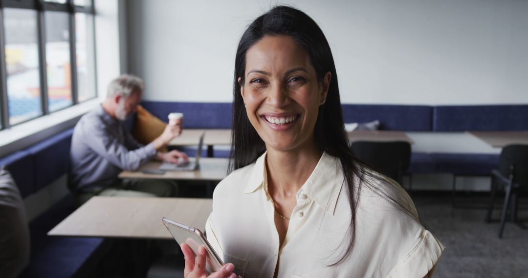 Confident Woman Smiling While Holding Smartphone in Modern Office - Free Images, Stock Photos and Pictures on Pikwizard.com