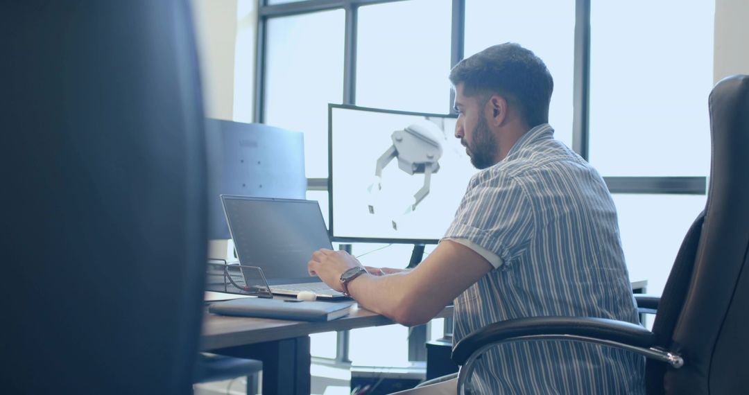 Engineer Designing 3D Robotic Arm on Laptop and Monitor