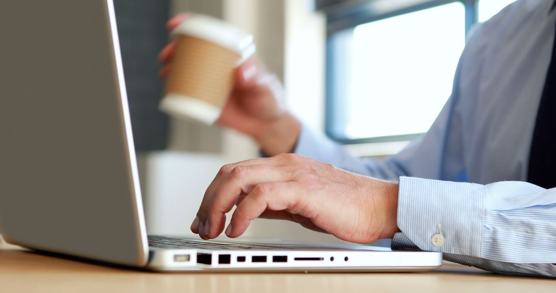 Businessman Working on Laptop and Holding Coffee Cup - Free Images, Stock Photos and Pictures on Pikwizard.com