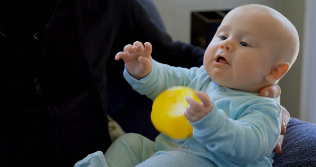 Curious Baby Playing with Yellow Ball While Sitting on Parent's Lap - Free Images, Stock Photos and Pictures on Pikwizard.com