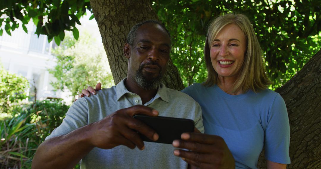 Diverse senior couple in garden taking selfie sitting under a tree and smiling - Free Images, Stock Photos and Pictures on Pikwizard.com