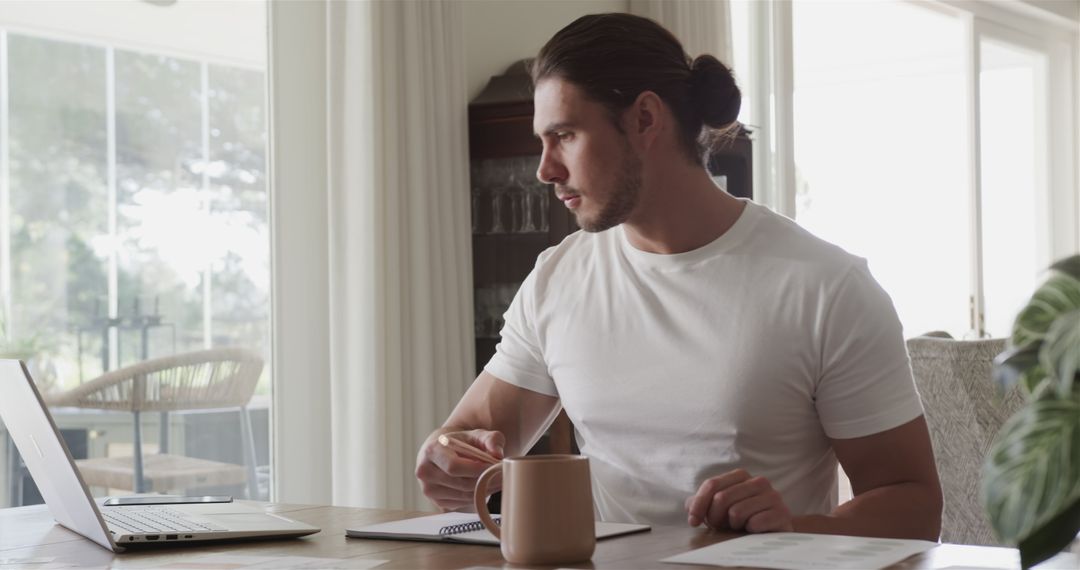 Focused Man Working Remotely on Laptop with Coffee at Home Office