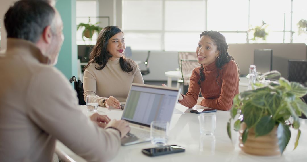 Diverse team collaborating in bright office around laptop with woman leading discussion