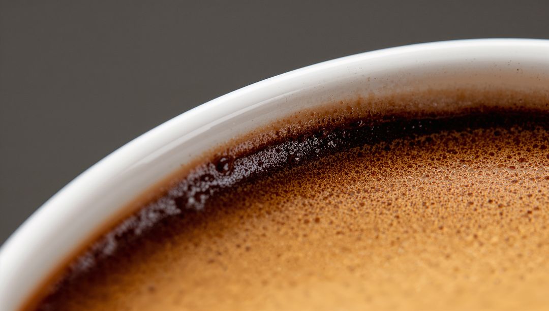 Macro espresso crema close-up showing white ceramic cup rim and frothy coffee texture