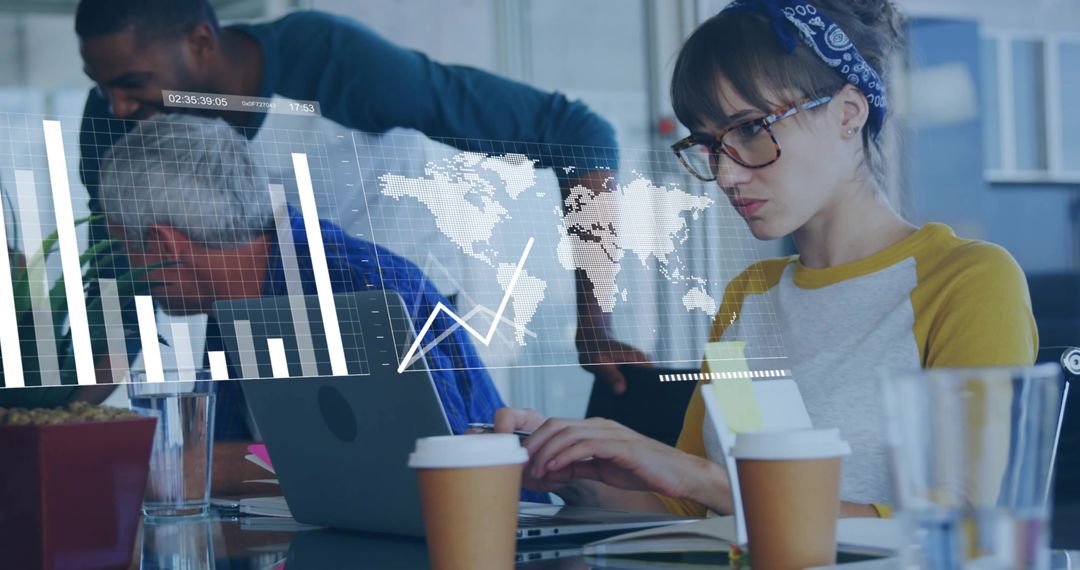 Young woman analyzing global data on laptop while team collaborates in office workspace