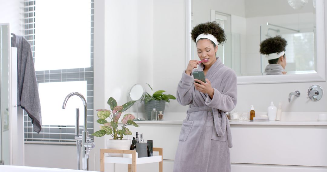 Smiling Woman Brushing Teeth While Using Smartphone in Modern Bathroom - Free Images, Stock Photos and Pictures on Pikwizard.com