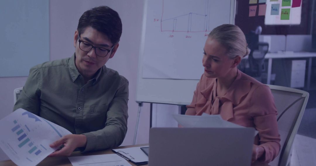Coworkers reviewing charts and planning project strategy during collaborative office meeting