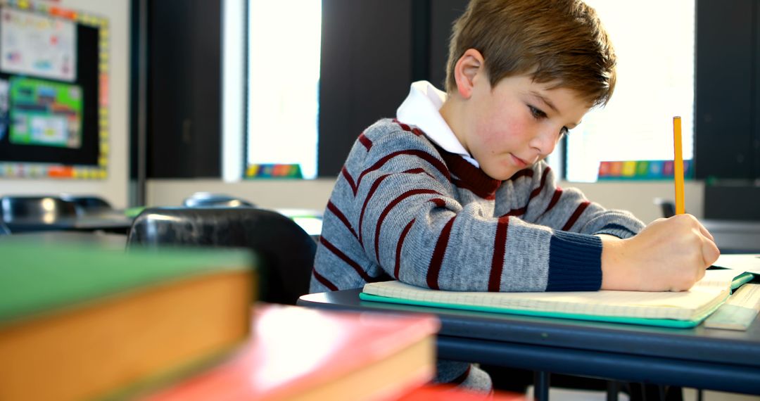 Young Boy Writing in Classroom Setting with Notebooks