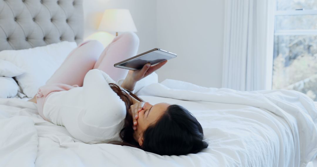 Woman Relaxing on Bed While Using Tablet in Bright Bedroom - Free Images, Stock Photos and Pictures on Pikwizard.com