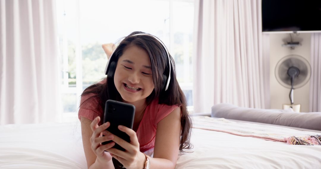 Smiling Woman Wearing Headphones Using Smartphone in Bedroom