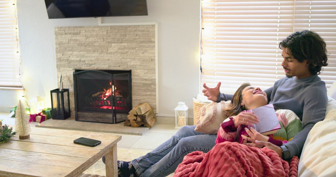 Couple cuddling on sofa by fireplace holding book and cozy chunky knit blanket