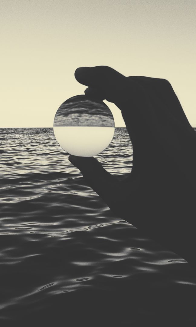 Hand Holding Glass Ball Reflecting Calm Ocean Sunset Landscape - Free Images, Stock Photos and Pictures on Pikwizard.com